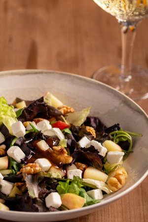 Mediterranean cuisine salad with lettuce, apple, goat cheese and walnuts with glass of wine on wooden tableの写真素材