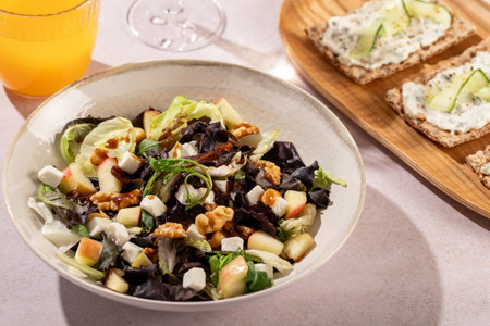 A fresh salad with feta, walnuts, apples, and crackers with cucumber and tsasiki, accompanied by orange juiceの写真素材