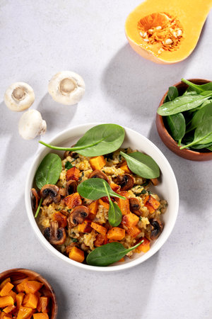 A vegan risotto with roasted pumpkin, mushrooms, and fresh spinach served in a white bowl on a light background, top viewの写真素材