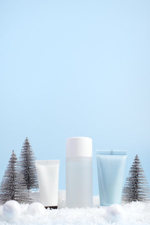 Winter skincare beauty concept with cosmetic products and holiday-themed decorations on a blue background, front view, copy spaceの写真素材