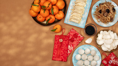 Traditional Chinese New Year food arrangement frame on a table, featuring dumplings, noodles, oranges with red envelopes for gifts, top view, copy spaceの写真素材
