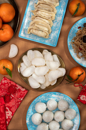 Chinese New Year food arrangement on a table, featuring dumplings, noodles, oranges with red envelopes for giftsの写真素材