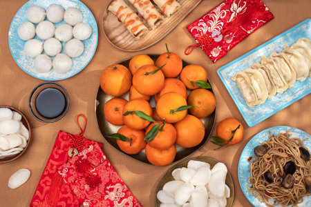 Chinese New Year food arrangement on a table, featuring dumplings, noodles, oranges with red envelopes for giftsの写真素材