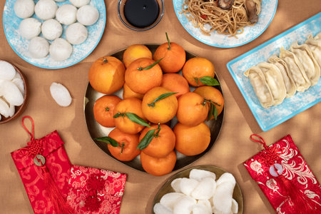 Chinese New Year food arrangement on a table, featuring dumplings, noodles, oranges with red envelopes for giftsの写真素材