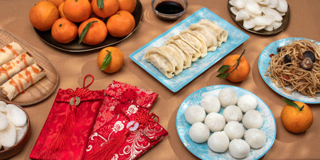 Chinese New Year food arrangement on a table, featuring dumplings, noodles, oranges with red envelopes for giftsの写真素材