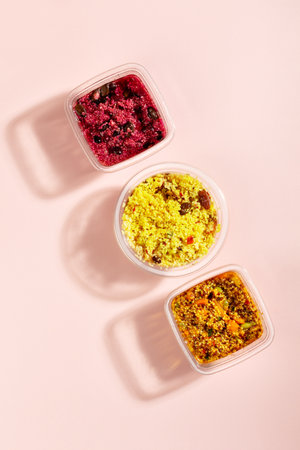 Premade quinoa and bulgur salads with vegetables and sauce on pink table. Quick food to eat on the go or for lunch break, time saving ready to eat healthy gluten free and vegan mealsの写真素材