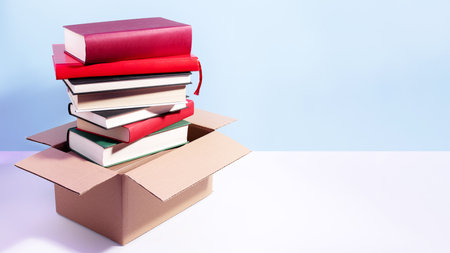 Used second-hand books in a box ready for donation against a blue background, minimal style still life. Concept of books donations, educational charity, copy spaceの写真素材