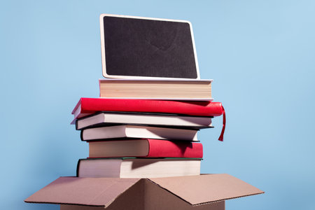 Used second-hand books in a box ready for donation with empty sign for text against a blue background, minimal style still life. Concept of books donations, educational charity, copy spaceの写真素材