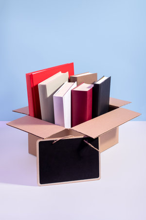 Used second-hand books in a box ready for donation with empty sign for text against a blue background, minimal style still life. Concept of books donations, educational charity, copy spaceの写真素材
