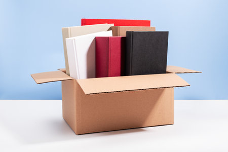 Used second-hand books in a box ready for donation against a blue background, minimal style still life. Concept of books donations, educational charity, copy spaceの写真素材