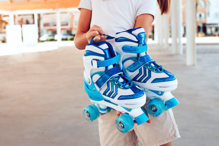 Young girl holding blue roller skates in park, copy space.の写真素材