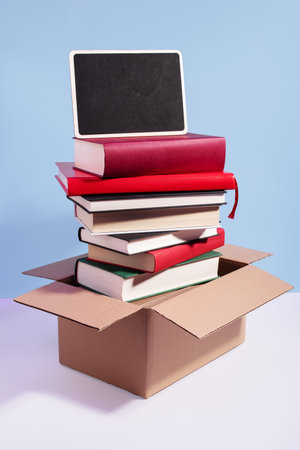 Used second-hand books in a box ready for donation with empty sign for text against a blue background, minimal style still life. Concept of books donations, educational charity, copy spaceの写真素材