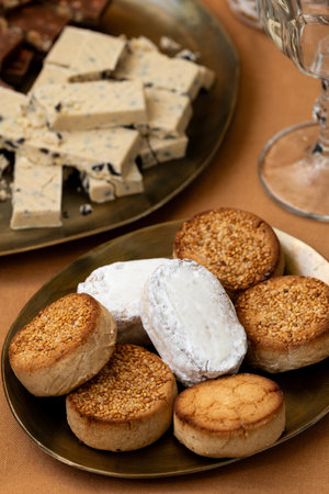 A close-up of traditional Spanish sweets, including Polvorones and Mantecados with sesame, served on golden plates alongside nougat turron pieces on a festive tableの写真素材