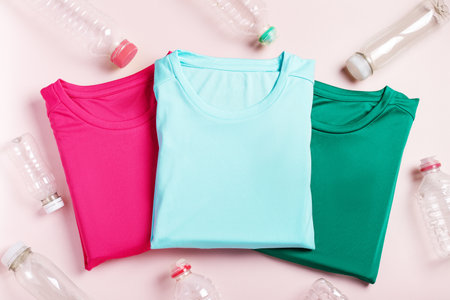 Plastic bottles and t-shirts on pink, concept of clothing production from recycled plastic materials, top viewの写真素材