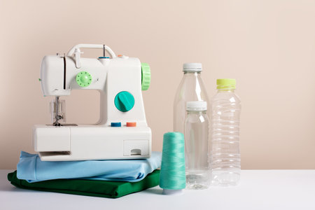 Plastic bottles, sewing machine, folded t-shirts still life, copy space, concept of clothes made from recycled plasticの写真素材