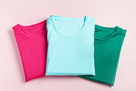 Three folded plain t-shirts in pink, light blue, and green laid out on a pastel pinkの写真素材