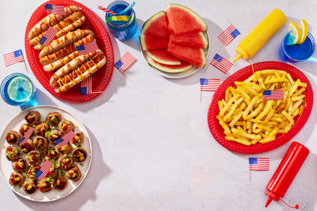 Top view of patriotic American food with hot dogs, fries, meatballs, watermelon, and drinks decorated with USA flags, copy spaceの写真素材
