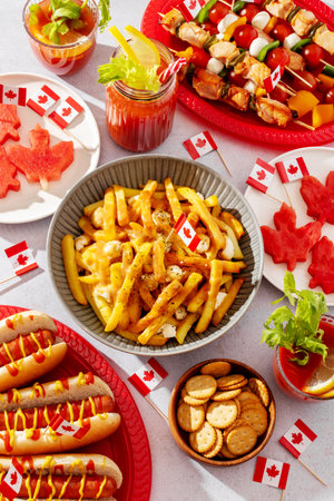 Top view of Canada Day party food with poutine, hot dogs, fruit, skewers, and donuts decorated with Canadian flags on a light background.の写真素材