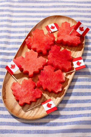 Maple leaf-shaped watermelon slices with Canadian flags on a wooden tray for Canada Day celebrationの写真素材
