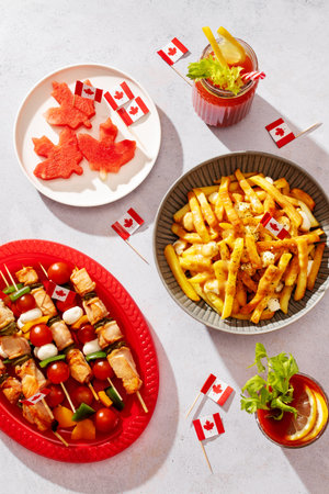 Top view of Canada Day party food with poutine, fruit, skewers, and crackers decorated with Canadian...