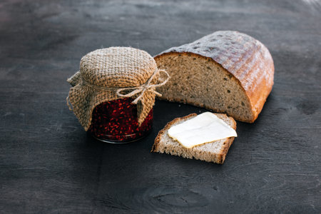 Lunch breakfast. Raspberry jam in a jar and bread with butter on the dark wooden background