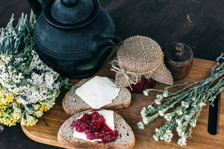 Raspberry jam and bread with butter in a jar and hot herbal tea on the wooden table Lunch breakfast