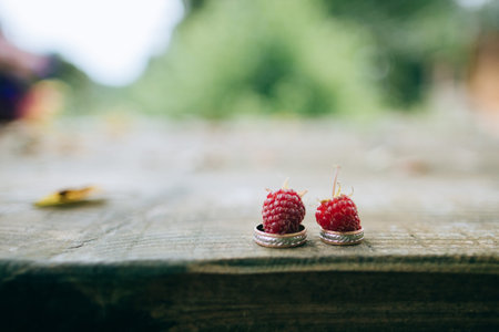 Golden wedding rings with raspberries on background of wood table