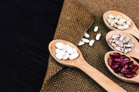 Colorful dry beans in wooden spoons on old clothの写真素材