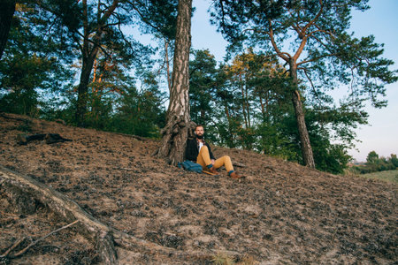 Young bearded hipster man relaxing sitting under a tree in the forest. Travel conceptの写真素材