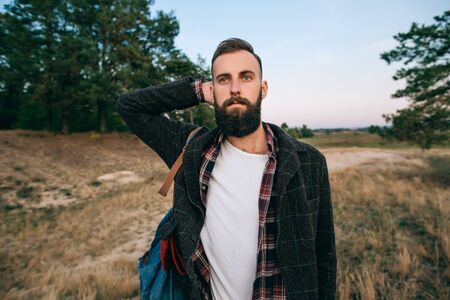 beautiful portrait of a young bearded man standing in the woods looking into the valleyの写真素材