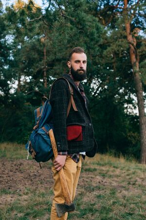 Hipster portrait brutal bearded and moustached woodcutter Gypsy man in the forest with ax. Travel styleの写真素材