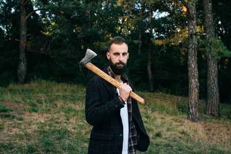 Portrait of young bearded hipster logger with ax in forestの写真素材