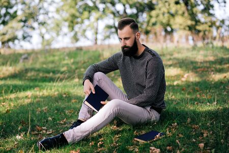 Handsome Young bearded student man hipster reading book in park on a summers sunny dayの写真素材