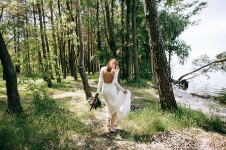 bride in a white dress walking in the woods by the sea beach. wedding concept	の写真素材