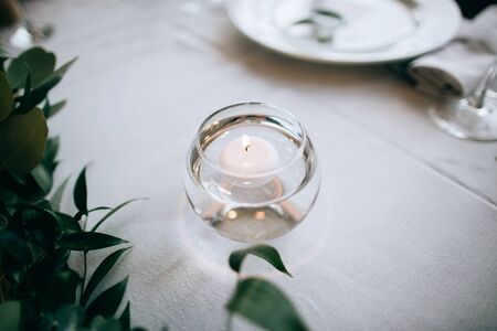 Beautiful decor on the table for the festive dinner: white tablecloth, candles, green branchesの写真素材