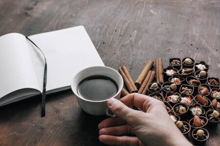 Cup of coffee in man hand with chocolate candies and a Notepad on wooden background. Work and relax space concept	
の写真素材