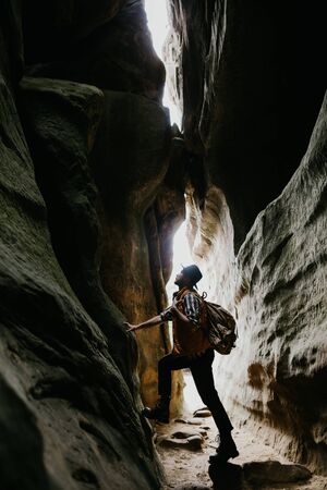 Young man tourist with a backpack explores a mountain cave, wanderlust conceptの写真素材