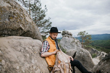 A young man in a hat sits on top of a cliff and looks around. Travel concept