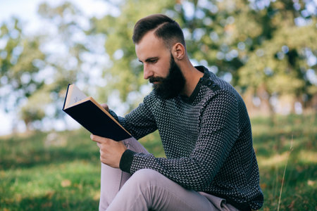 Student hipster bearded man reading a book outdoors
