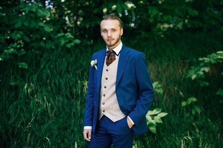 Groom portrait in a blue suit in forest at a wedding day	の写真素材