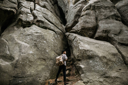 A hiker stands in front of a high cliff obstacle. Mountain tourism