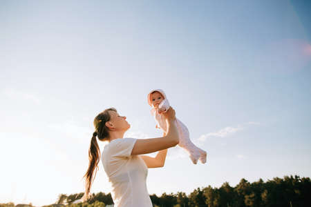 A mother holds her daughter in her arms and kisses her tenderly in the sun. The concept of motherhoodの写真素材