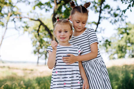 Little girl crying outdoors. The older sister takes care of her younger sister. Girlfriendsの写真素材