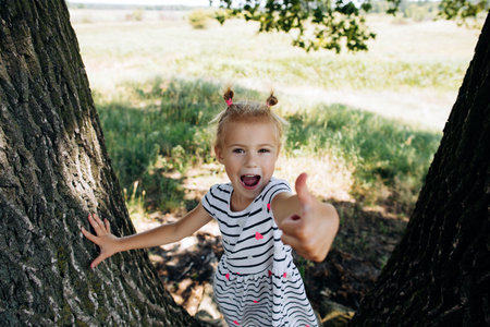 Happy girl showing thub up in a summer park. Children's vacation