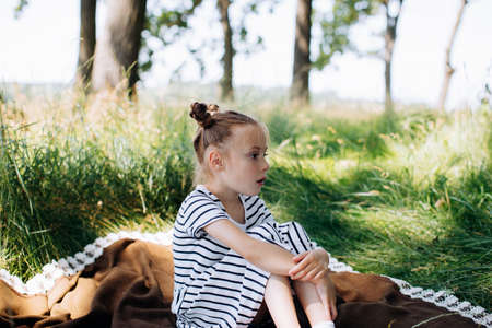Little girl in a striped dress sitting on a blanket in a summer parkの写真素材