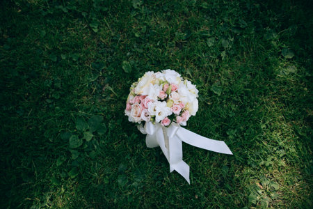 Wedding bouquet of white and pink roses lies on the green grass. Wedding accessories