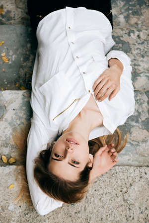 Outdoors portrait of beautiful young sensual woman looking at camera and lies on the stairsの写真素材