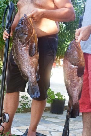 Two people cleaning two groupers