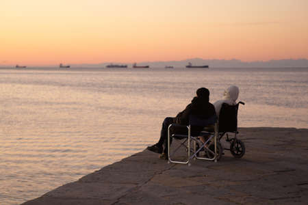 Disabled person in a wheelchair and his friend looking the seaの写真素材