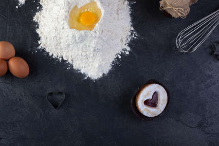 Pastry cookie with a red jam heart and icing powder sugar and cooking utensils on tableの写真素材